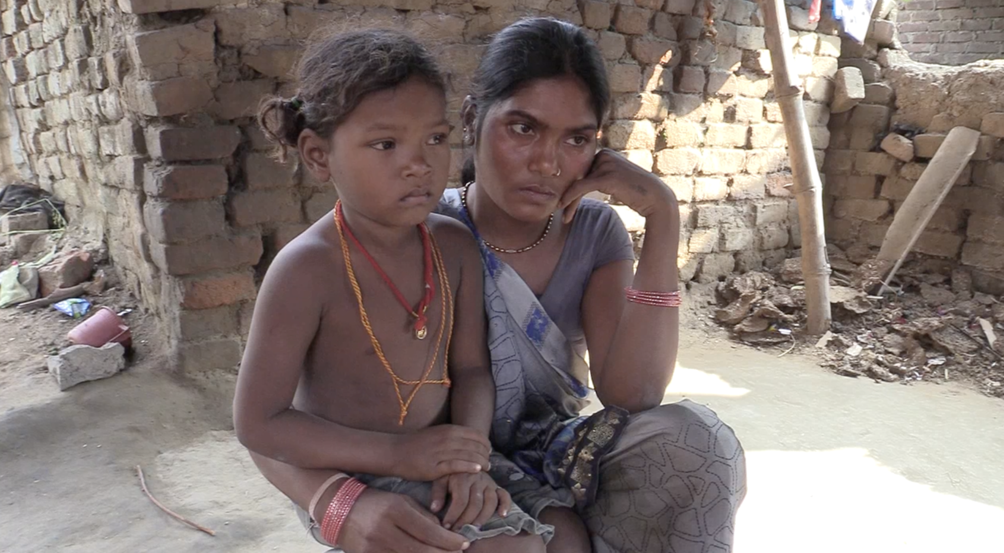 A woman sitting with a child on her lap in a visibly impoverished house