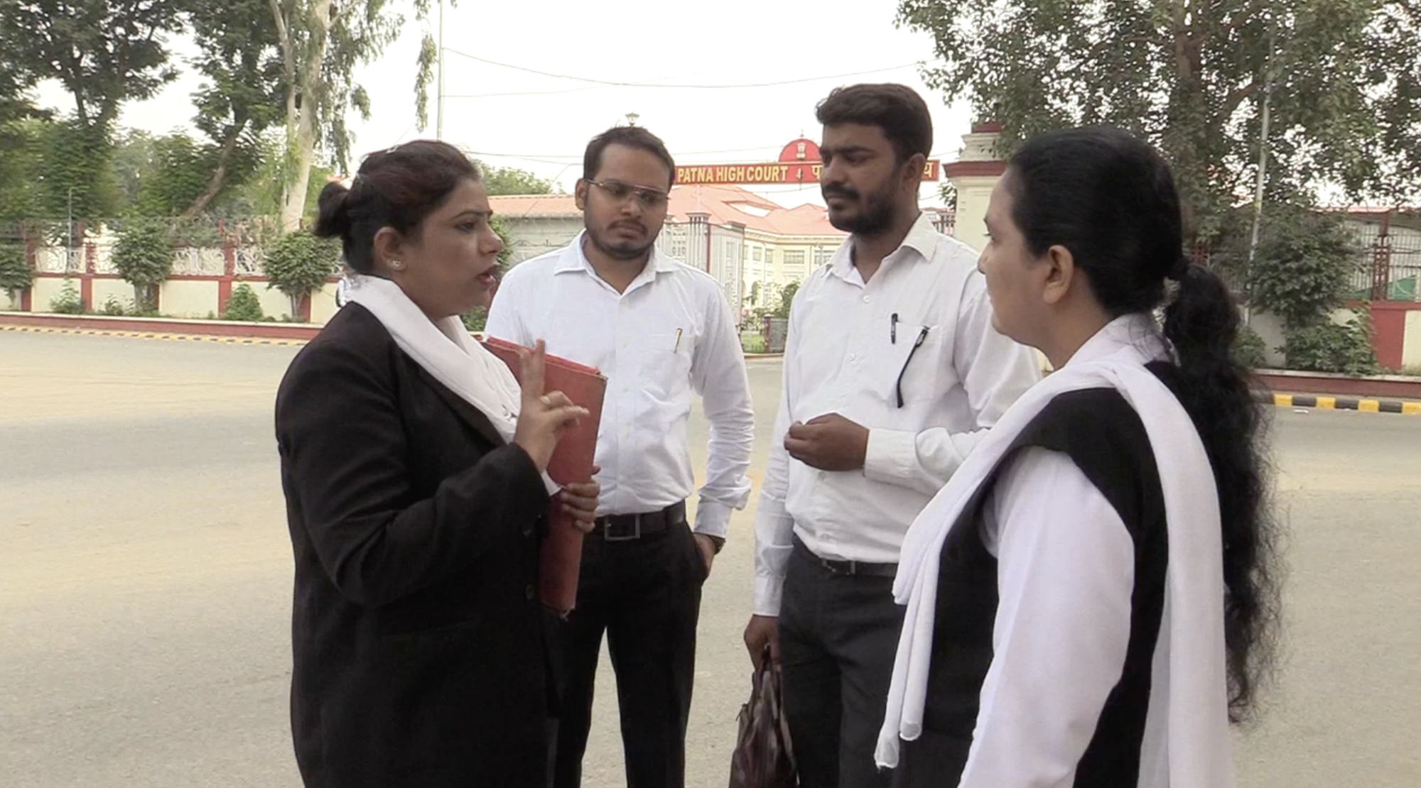 Two women and two men in lawyer attire standing on the road. Savita is explaining something to her colleagues