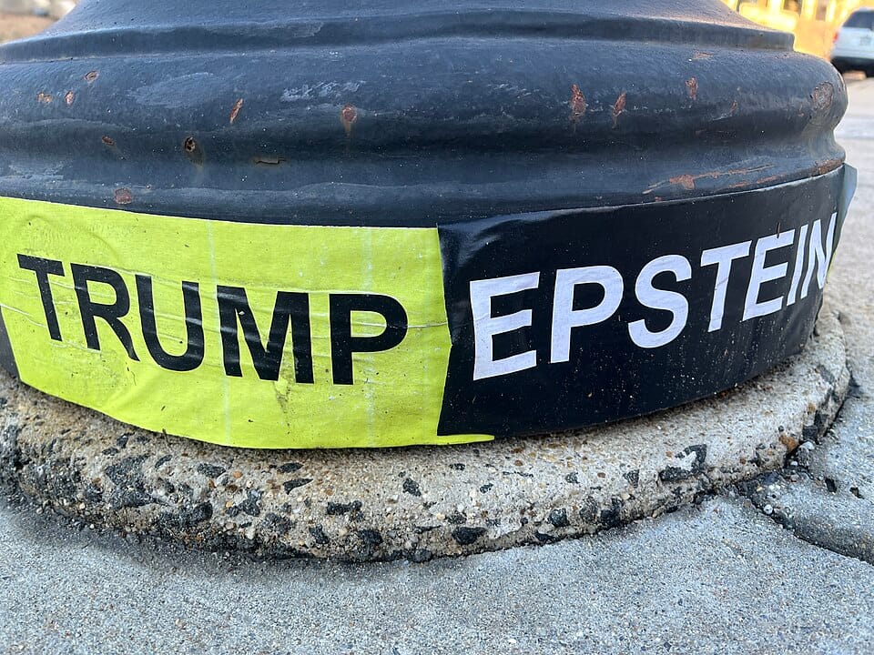 The black round base of a street light in closeup with "Trump" written against a yellow background and "Epstein" written against a black background.