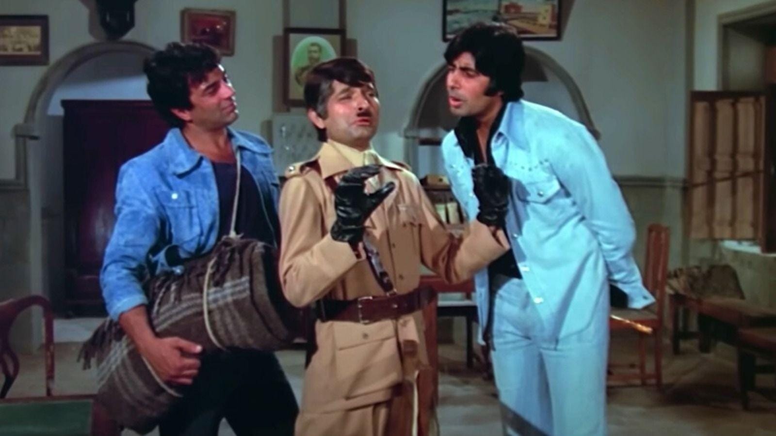 Indoor scene from the film Sholay in what looks like a police station. Dharmendra and Amitabh Bachchan are flanking Asrani who has a toothbrush moustache. He is in a khakhi police uniform, black gloves, and a wide belt.