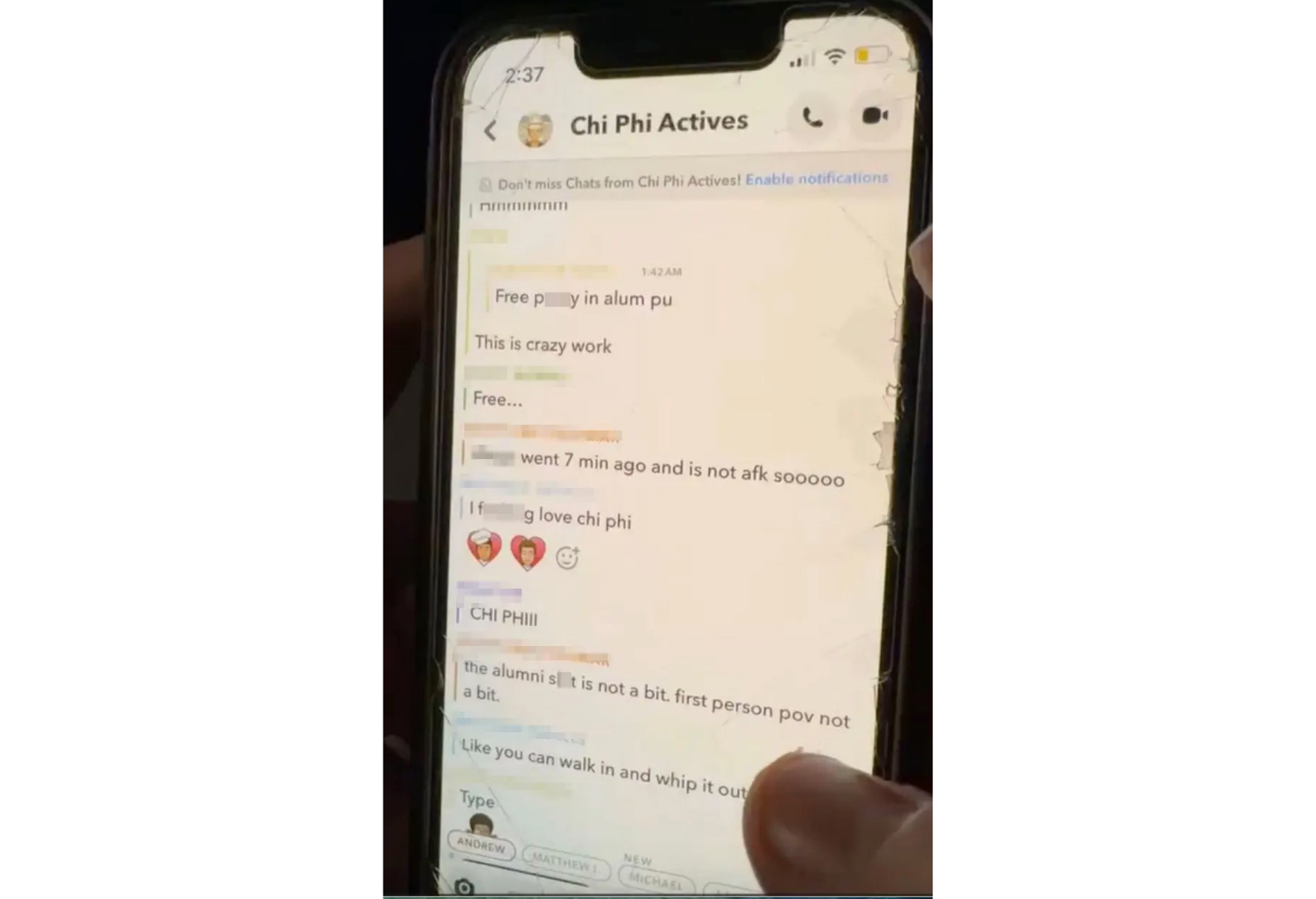 A photo of a smartphone with a thumb holding the phone showing on the left. The screen looks old and shattered on the edges. The text exhanges on a group called "Chi Phi Actives" are shown. The names have been redacted by the owner of the image.